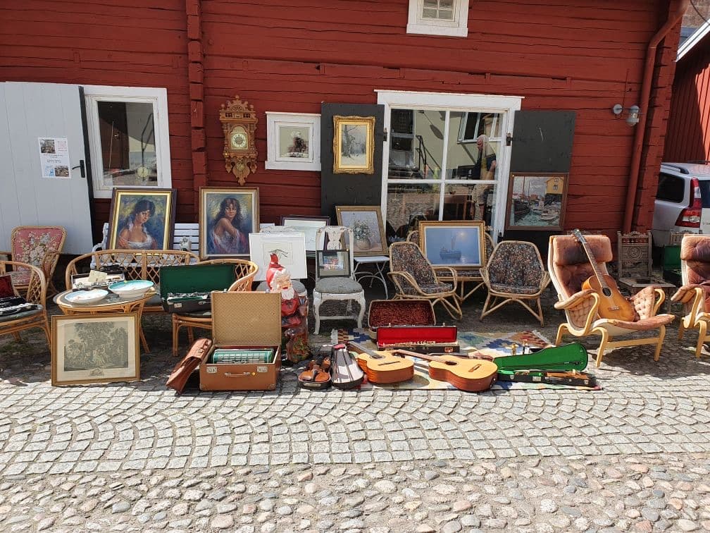 Antikviteter uppställda utanför Skaraborgs Antiks butik – tavlor, stolar, resväskor och gitarrer på en kullerstensgata