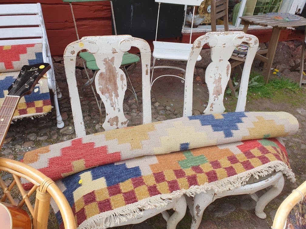 Vittrade vintagestolar och rullade kilimmattor utställda utomhus utanför butiken